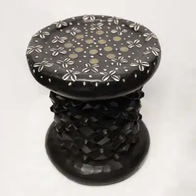 Taburete africano vintage de color negro: obra de arte de madera hecha a mano decorada con monedas y cauris disponible en Baobabmart